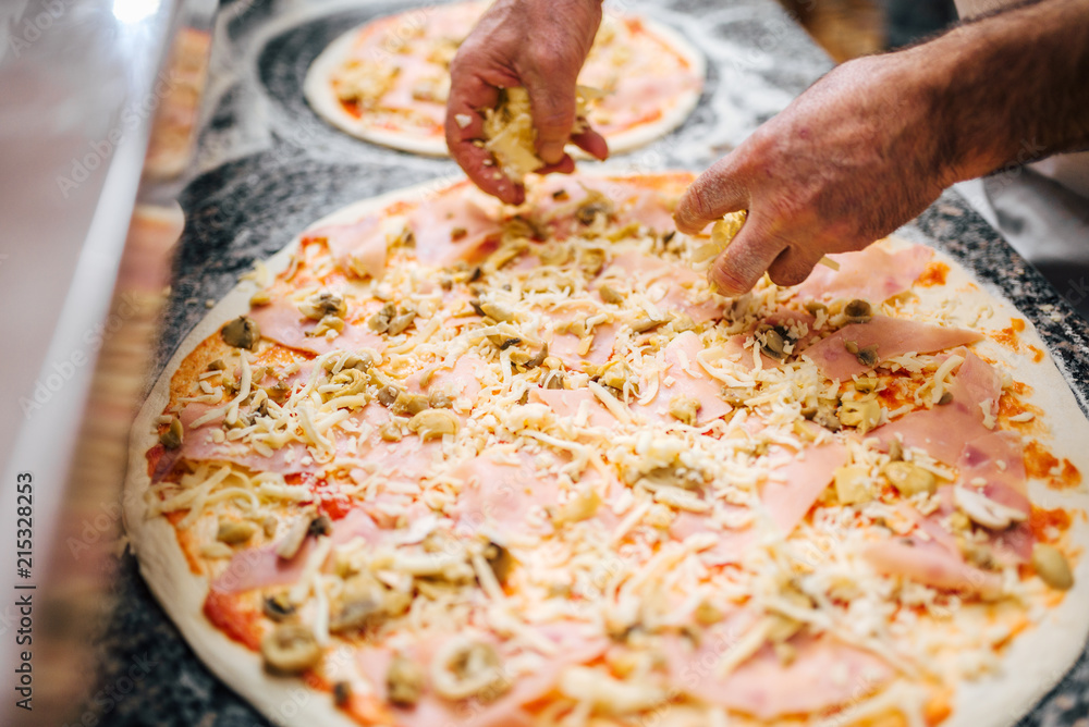Chef adding cheese on unbaked pizza. Close-up.