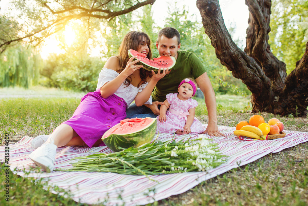 Family at picnic. Parents eating a watermelon. Baby girl looking at camera.