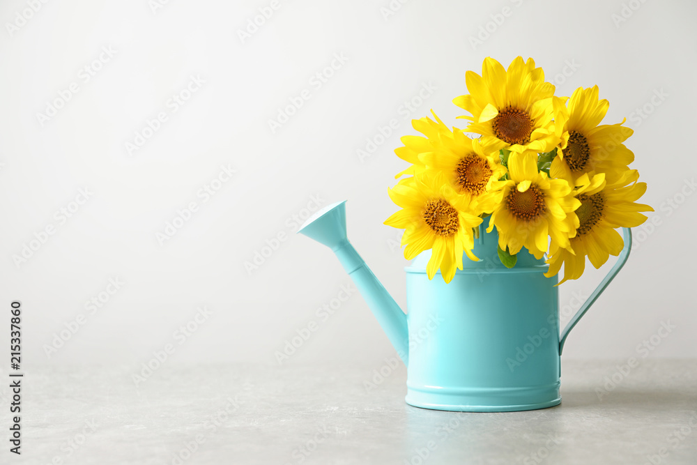 Watering can with beautiful yellow sunflowers on table