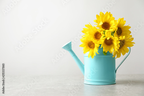 Fototapeta Naklejka Na Ścianę i Meble -  Watering can with beautiful yellow sunflowers on table