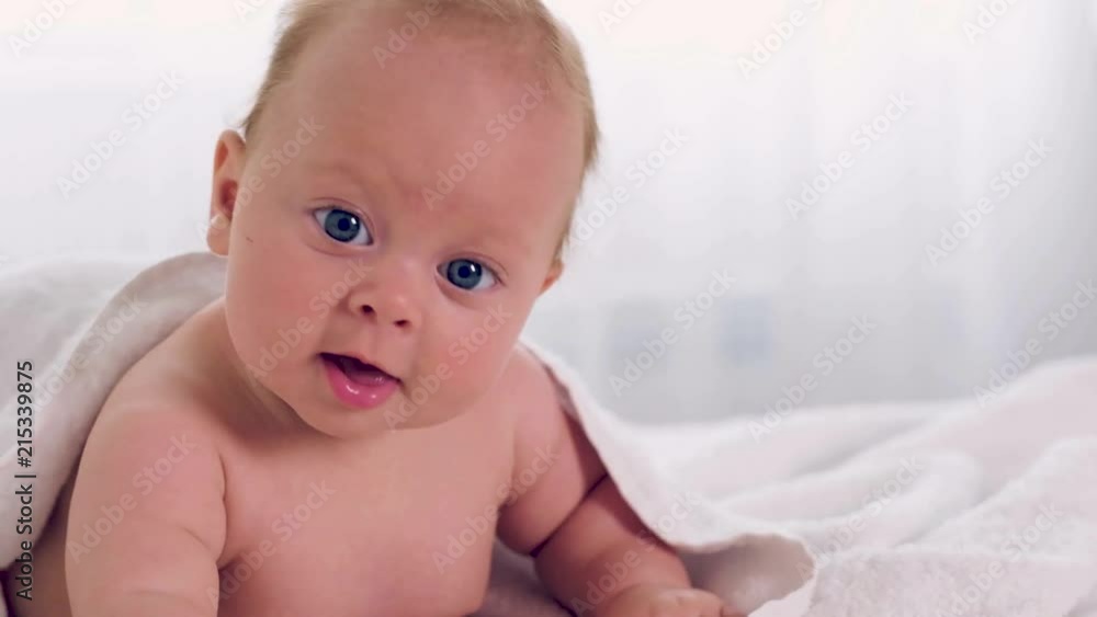 Happy smiling baby under the soft white towel. Newborn baby after bath covered with blanket Happy smiling baby under the soft white towel. Newborn baby after bath covered with blanket