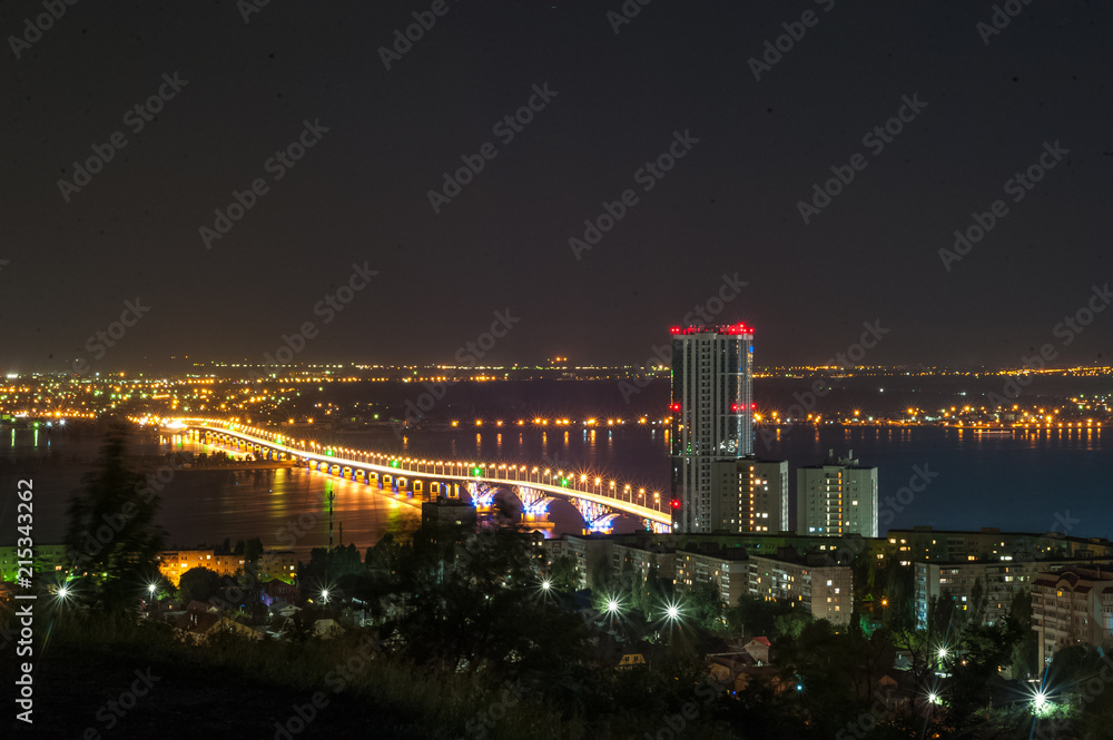 Moon eclipse. View of the night city of Saratov, Russia. The lights of a metropolis in the night. View of the bridge over the Volga River.