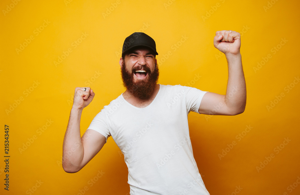 Portrait of a satisfied young bearded man in white t-shirt celebrating success isolated over yellow background Portrait of a satisfied young bearded man in white t-shirt celebrating success isolated over yellow background