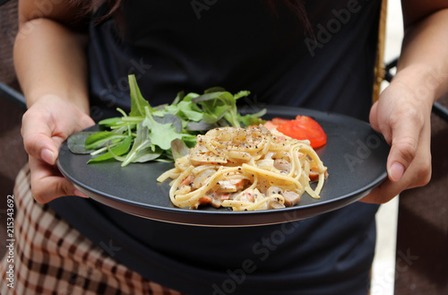 The Spaghetti Carbonara with green vegetable and red tomatoes cut into pieces in hands to serve.