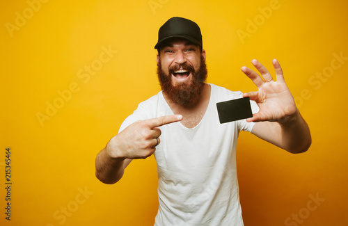 Portrait of a cheerful bearded man pointing finger at credit card isolated over yellow background