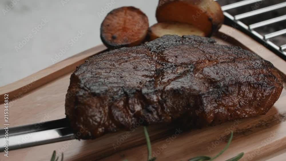 A grilled steak turned on another side is moved from the grill to a served wooden board in slow motion A grilled steak turned on another side is moved from the grill to a served wooden board in slow motion