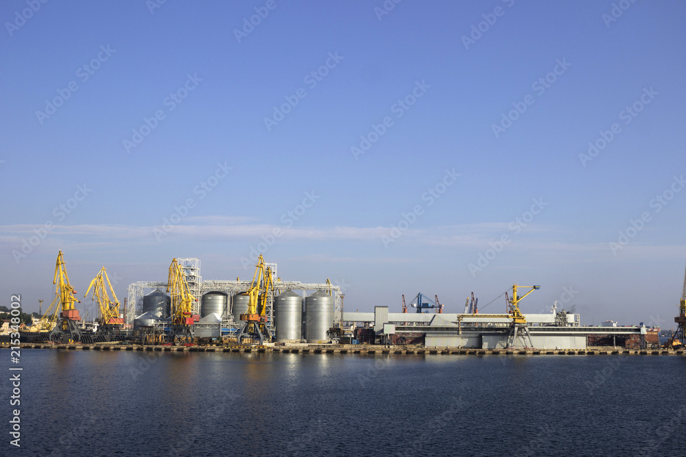 Cranes and granaries, cisterns with wheat in the port in clear weather, the sea.