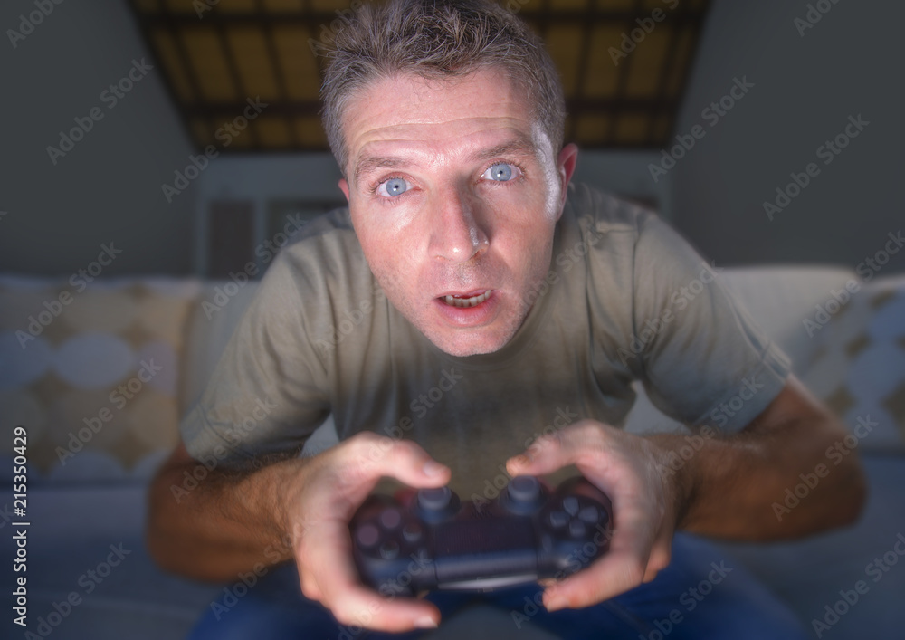 lifestyle portrait of young stressed and excited gamer man playing video game at home living room having fun on sofa couch holding controller concentrated lifestyle portrait of young stressed and excited gamer man playing video game at home living room having fun on sofa couch holding controller concentrated
