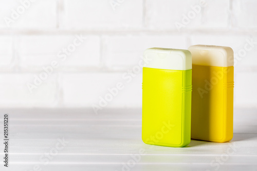 Two closed plastic shampoo and conditioner containers, green and yellow, on white background. Copy space