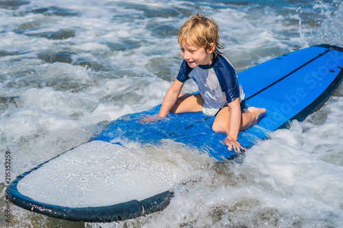 Happy baby boy - young surfer ride on surfboard with fun on sea waves. Active family lifestyle, kids outdoor water sport lessons and swimming activity in surf camp. Summer vacation with child photo