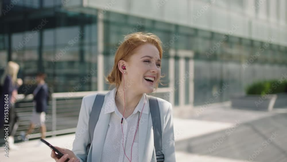 portrait of cheerful red head business woman executive wearing earphones listening to music texting browsing using smartphone social media app laughing reading messages portrait of cheerful red head business woman executive wearing earphones listening to music texting browsing using smartphone social media app laughing reading messages