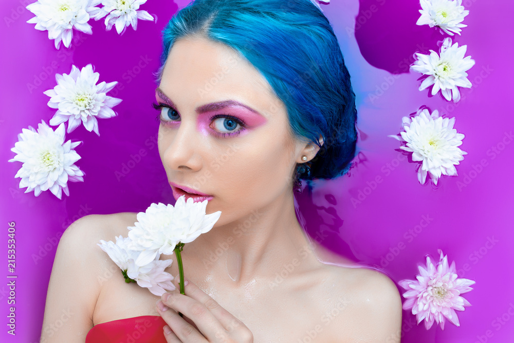 Portrait of young pretty female girl adult woman / fashion luxury model with blue hair relaxing in bathtub isolated by pink water with white flowers. Organic skin care, beauty and body care concept. Portrait of young pretty female girl adult woman / fashion luxury model with blue hair relaxing in bathtub isolated by pink water with white flowers. Organic skin care, beauty and body care concept.