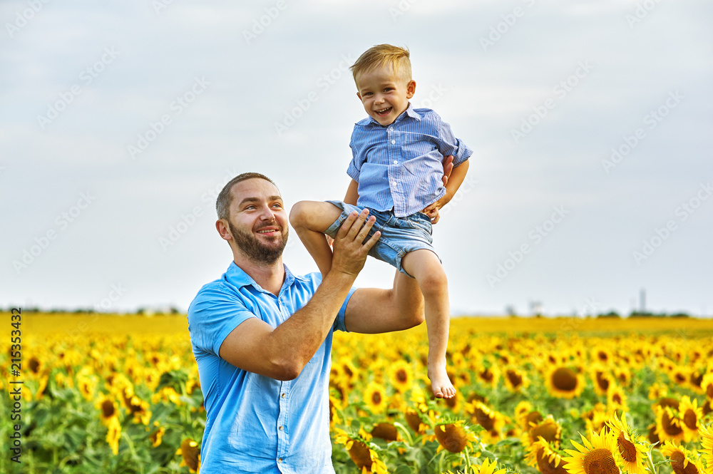 Cheerful loving father with his son on vacation in the field with sunflowers . The parent plays with his son . Father's day Cheerful loving father with his son on vacation in the field with sunflowers . The parent plays with his son . Father's day