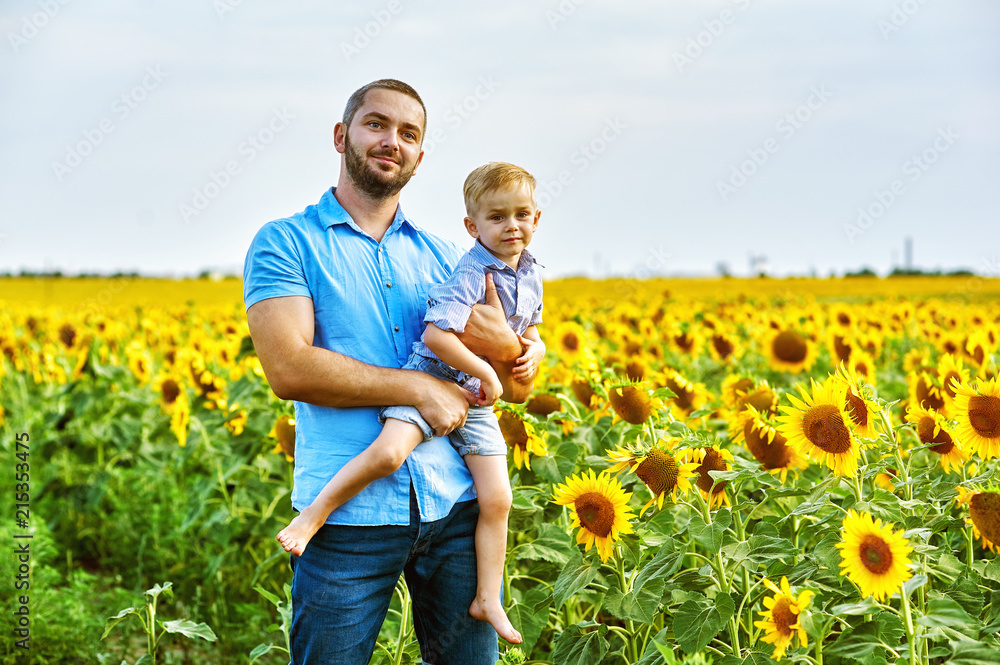Cheerful loving father with his son on vacation in the field with sunflowers . The parent plays with his son . Father's day Cheerful loving father with his son on vacation in the field with sunflowers . The parent plays with his son . Father's day