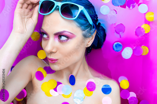 Portrait of young pretty female girl adult woman fashion luxury sexy model with blue hair relaxing wearing turquoise sunglsses in bath isolated by pink water with colorful confetti. Skin care, beauty