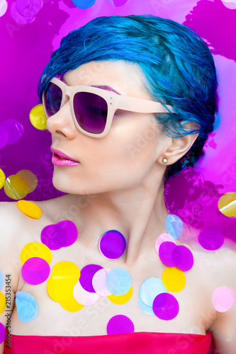Portrait of young pretty female girl adult woman fashion luxury sexy model with blue hair relaxing wearing pink sunglsses in bath isolated by pink water with colorful confetti. Skin and beauty care