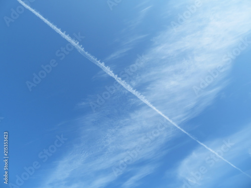 Blue sky with white cirrus clouds and airplane jet trail. Cloudscape as beautiful weather background