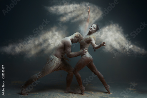 Dancing in flour concept. Girl woman female wearing white dress and guy man male making dance element in flour / white dust in form of wings as angels on isolated black / grey background