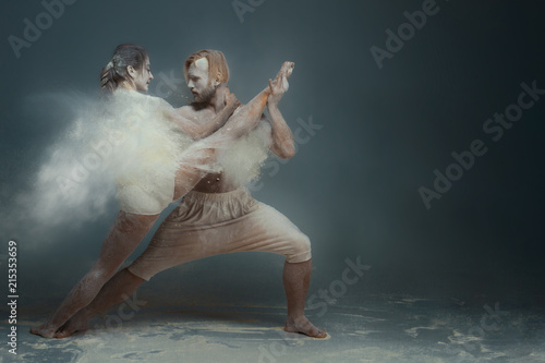 Fototapeta Naklejka Na Ścianę i Meble -  Dancing in flour concept. Girl woman female and muscle fitness guy man male couple in love and in relationship making dance element prefomance in flour / white dust on isolated black / grey background