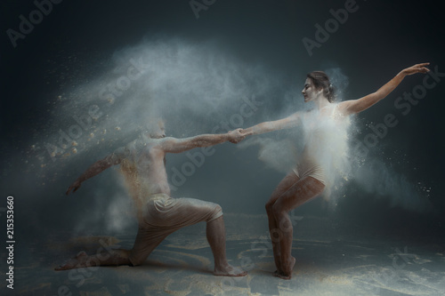 Dancing in flour concept. Girl woman female and muscle fitness guy man male couple in love and in relationship making dance element prefomance in flour / white dust on isolated black / grey background