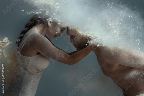 Dancing in flour concept. Girl woman female and muscle fitness guy man male couple in love and in relationship making dance element prefomance in flour / white dust on isolated black / grey background