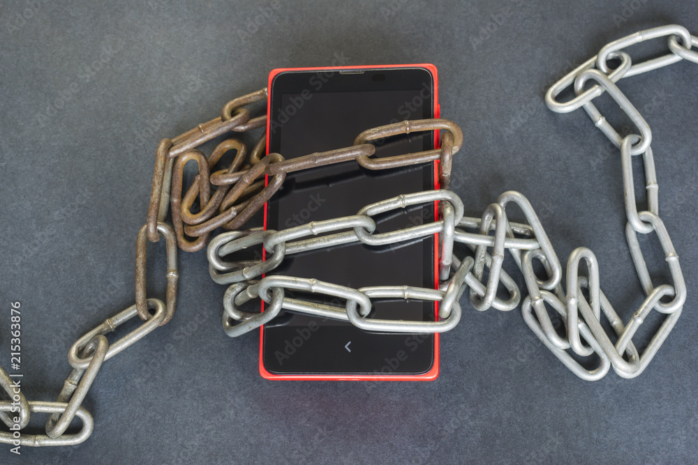 Technology addiction concept, smartphone and chains on the dark background. Technology addiction concept, smartphone and chains on the dark background.