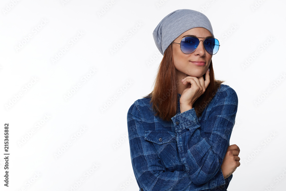 Telling joke to friend. Positive young good-looking European female student in hat and glasses, crossing hands together over chest and smiling joyfully, being in good mood while trying help customer. Telling joke to friend. Positive young good-looking European female student in hat and glasses, crossing hands together over chest and smiling joyfully, being in good mood while trying help customer.