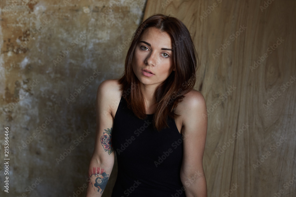 Beauty and human being. Authentic shot of natural mixed raced young tender woman with stylish haircut and dark sensual skin, looking at camera with serious and pensive expression against wooden wall. Beauty and human being. Authentic shot of natural mixed raced young tender woman with stylish haircut and dark sensual skin, looking at camera with serious and pensive expression against wooden wall.