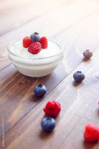 Yogurt in a glass transparent jar with fresh blueberries and raspberries on a wooden background.