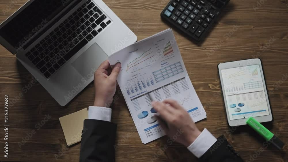 Top view businessman working at office desk with his laptop and tablet pc surrounded by a lot of paperwork and financial reports, notebooks. Business, people, paperwork concept