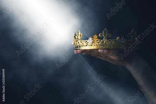 Foto mysteriousand magical image of woman's hand holding a gold crown over gothic black background