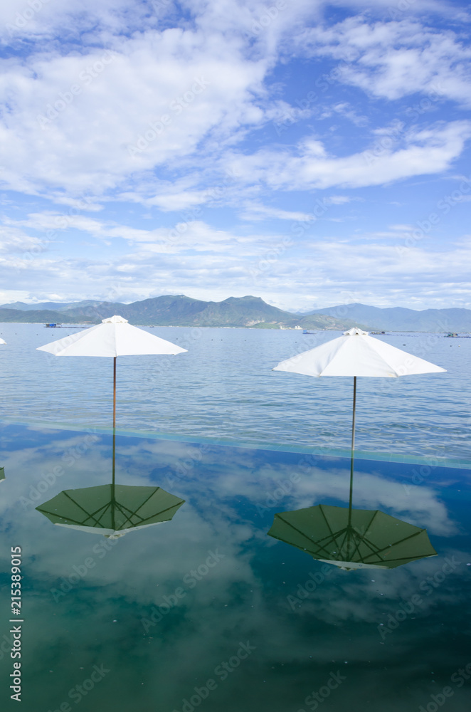 Beach umbrellas on the rim of an infinity pool at a tropical resort overlooking the calm ocean on summer day in a tourism and vacation concept