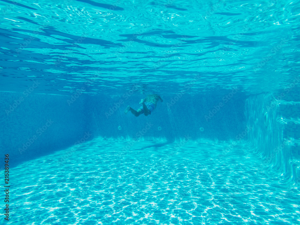 underwater image of an outside villa swimming pool with some steps at one side. A senior man is swimming at one end. The water is clear blue and the sunlight is making patterns
