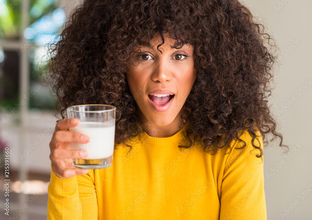 African american woman holding a glass of milk scared in shock with a surprise face, afraid and excited with fear expression African american woman holding a glass of milk scared in shock with a surprise face, afraid and excited with fear expression