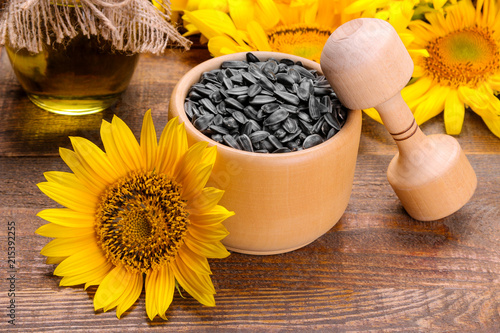 Sunflower seeds in a wooden crush and bright yellow sunflowers on a brown wooden background