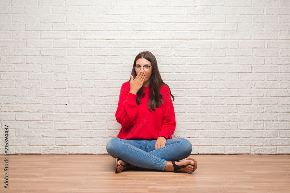 Young brunette woman sitting on the floor over white brick wall cover mouth with hand shocked with shame for mistake, expression of fear, scared in silence, secret concept Young brunette woman sitting on the floor over white brick wall cover mouth with hand shocked with shame for mistake, expression of fear, scared in silence, secret concept