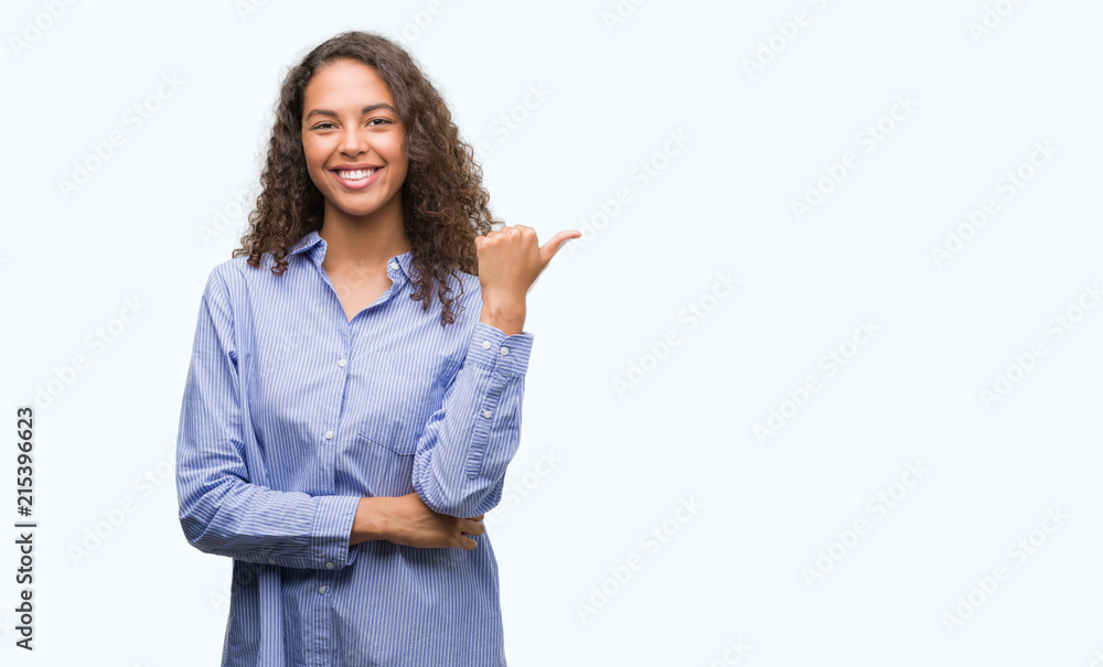 Young hispanic business woman smiling with happy face looking and pointing to the side with thumb up. Young hispanic business woman smiling with happy face looking and pointing to the side with thumb up.