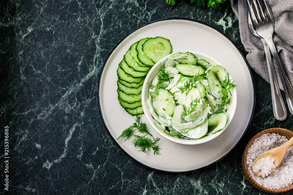 Obraz premium Creamy cucumber dill salad with yogurt dressing on dark marble background. Top view, space for text.