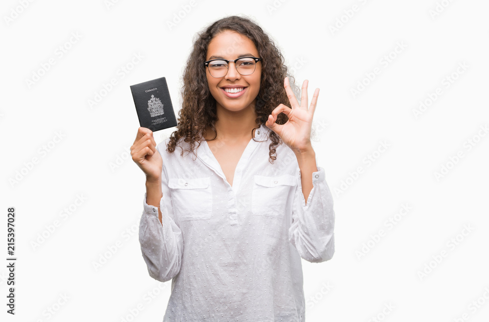 Young hispanic woman holding passport of Canada doing ok sign with fingers, excellent symbol Young hispanic woman holding passport of Canada doing ok sign with fingers, excellent symbol