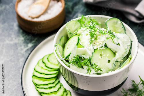 Creamy cucumber dill salad with yogurt dressing on dark marble background. Selective focus, space for text.