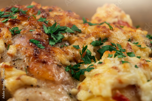 Chicken meat cooked in the oven with vegetables and a ruddy crust of cheese, decorated with chopped parsley.