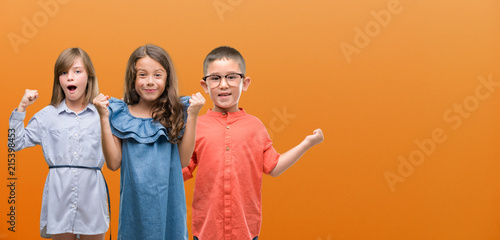 Group of boy and girls kids over orange background screaming proud and celebrating victory and success very excited, cheering emotion