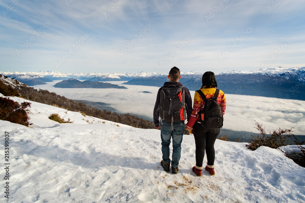 Couple holding hands standing on a high snowy mountain looking the ...