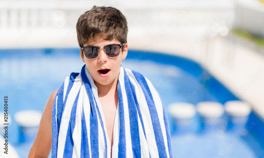 Young child on holidays at the swimming pool by the beach scared in shock with a surprise face, afraid and excited with fear expression Young child on holidays at the swimming pool by the beach scared in shock with a surprise face, afraid and excited with fear expression