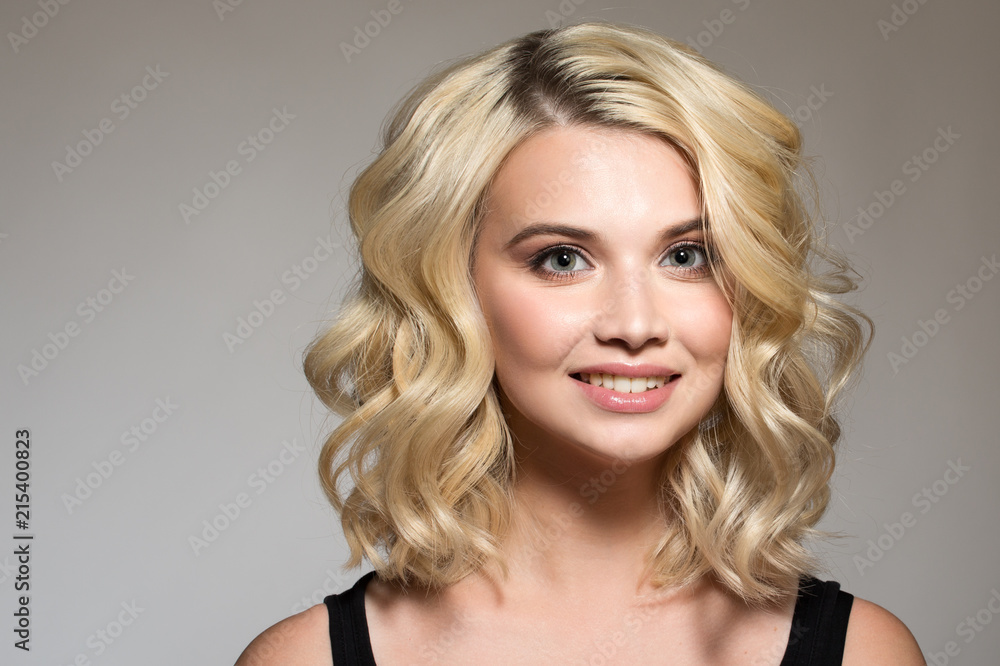 Blonde with curls on a gray background, natural make-up and clean skin. beautiful smile. Portrait Blonde with curls on a gray background, natural make-up and clean skin. beautiful smile. Portrait