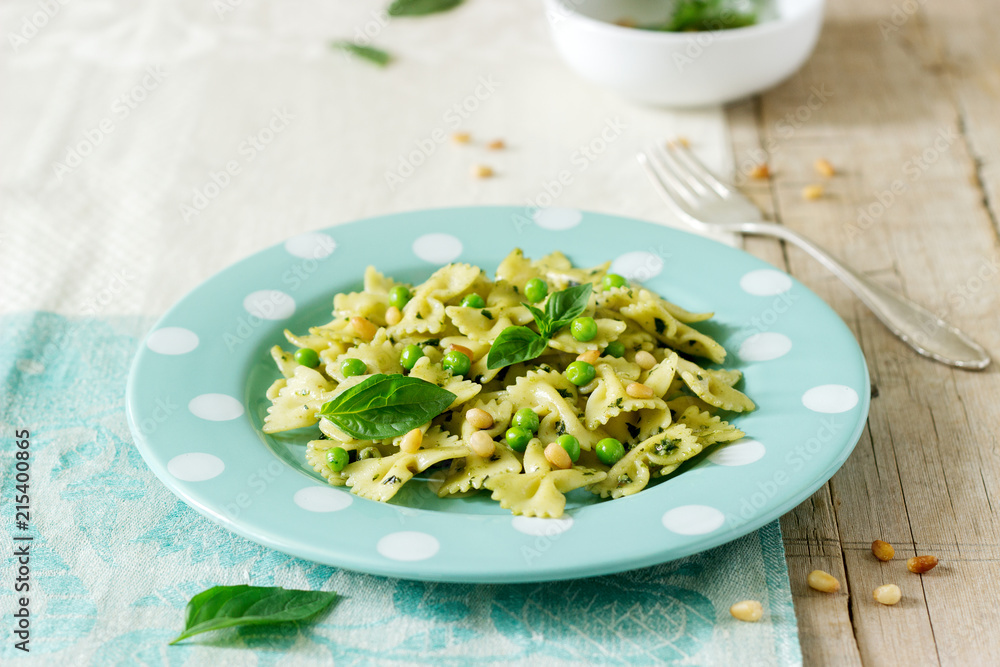 Pasta with pesto sauce, green peas and basil on a wooden table. Rustic style.