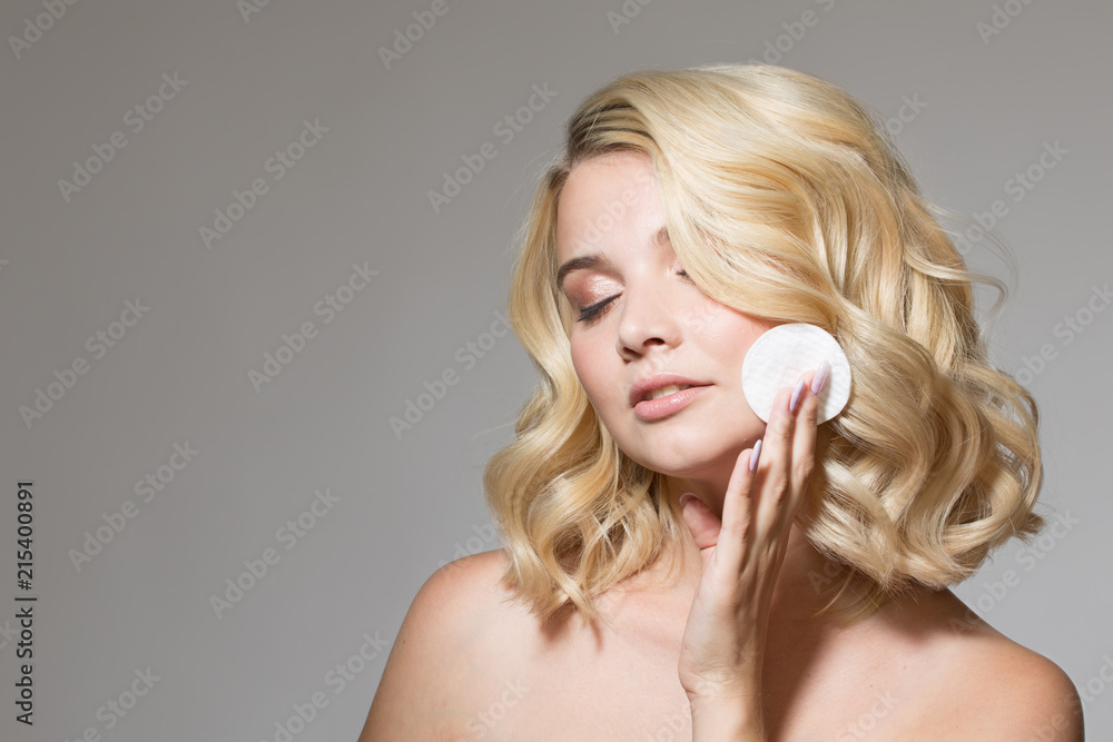 Blonde with curls on a gray background with a cotton disc in her hand. natural make-up and clean skin. Portrait woman Blonde with curls on a gray background with a cotton disc in her hand. natural make-up and clean skin. Portrait woman