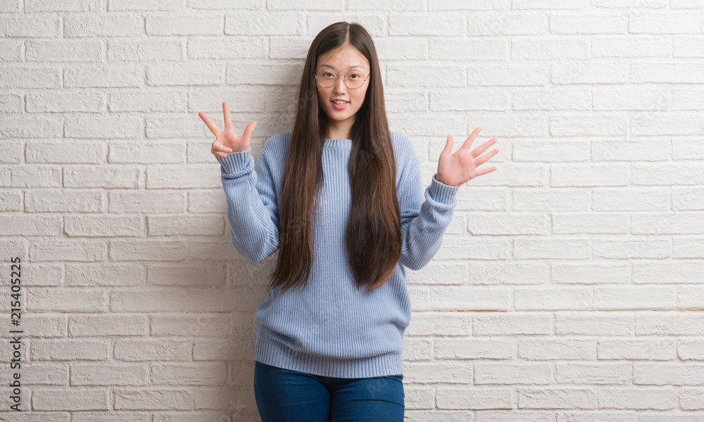 Young Chinise woman over white brick wall showing and pointing up with fingers number eight while smiling confident and happy. Young Chinise woman over white brick wall showing and pointing up with fingers number eight while smiling confident and happy.