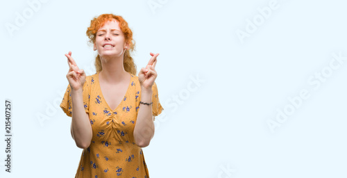 Young redhead woman smiling crossing fingers with hope and eyes closed. Luck and superstitious concept.