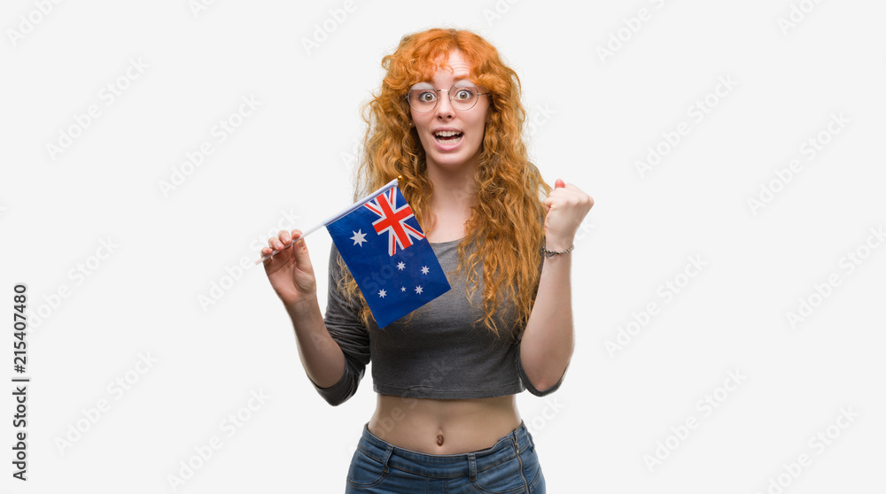 Young redhead woman holding flag of Australia screaming proud and celebrating victory and success very excited, cheering emotion Young redhead woman holding flag of Australia screaming proud and celebrating victory and success very excited, cheering emotion
